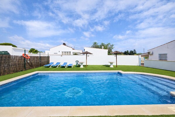 Une piscine avec des chaises longues, une petite table et un parasol en chaume.