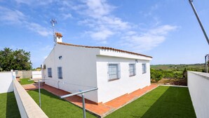 Un edificio blanco con techo de tejas, un pequeño jardín y una estructura metálica.