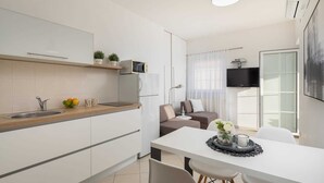 A modern kitchen with white cabinets, a wooden countertop, and a built-in microwave. There is a dining area with a white table and chairs, and a flat-screen TV mounted on the wall. - Apartment Arausa with Pool I (Vodice)