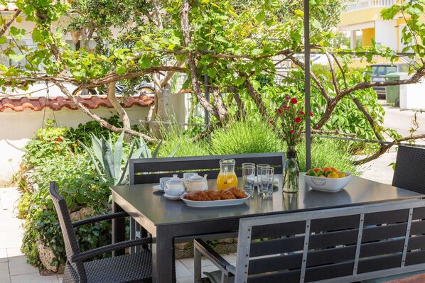 An outdoor dining table with a basket of croissants, a pitcher of orange juice, and a bowl of fruit. - Apartment Arausa with Pool I (Vodice)