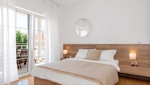 A bedroom with a bed, a wooden headboard, a round mirror, and a balcony with a table and chairs. - Apartment Arausa with Pool I (Vodice)