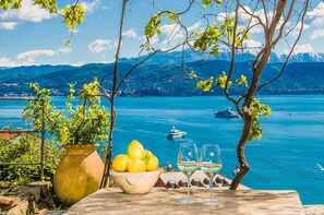 Una mesa con limones y copas de vino, con vistas a un lago con barcos y montañas al fondo.