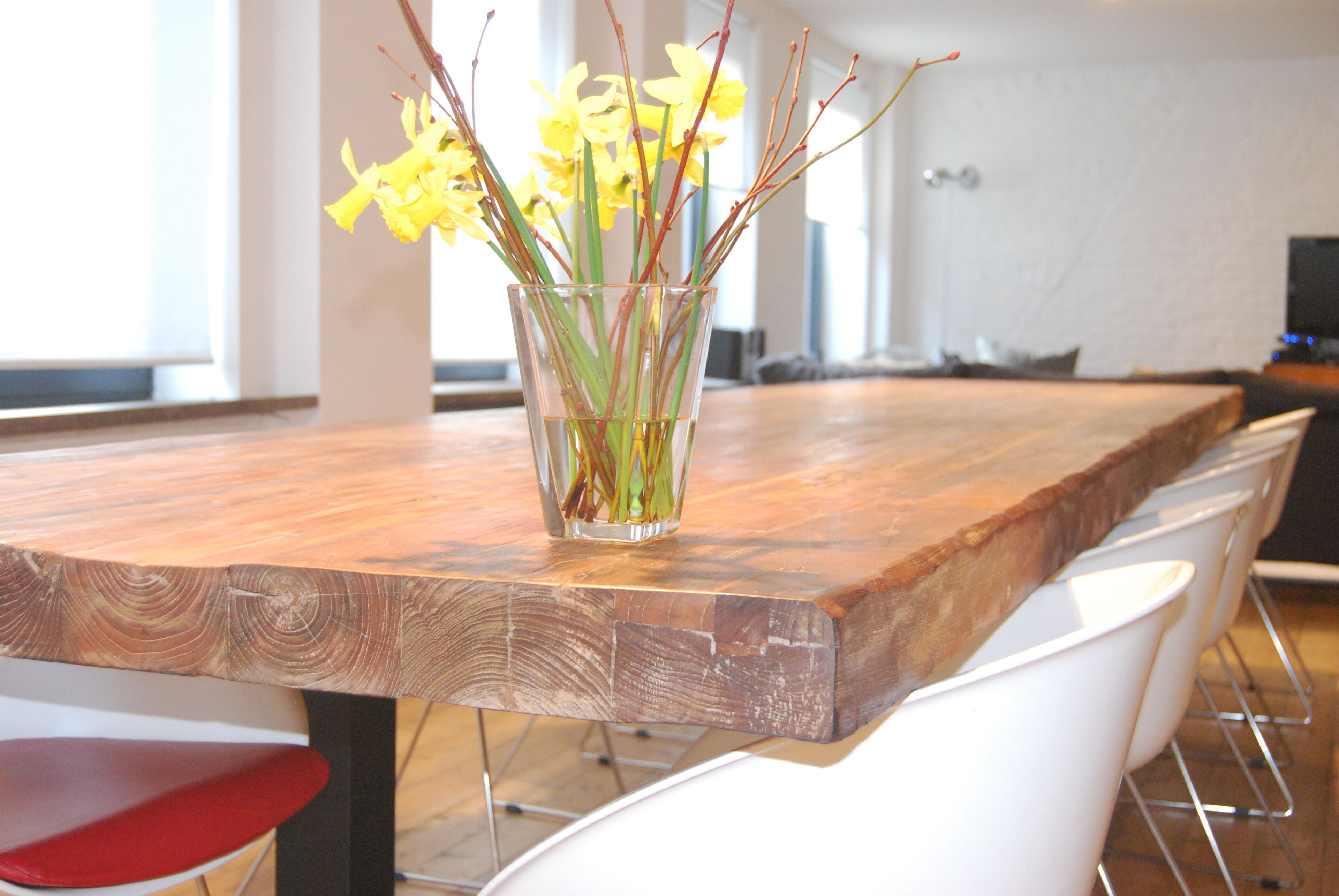 A wooden dining table with a glass vase of yellow flowers.
