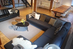Ein modernes Wohnzimmer mit einer Eckcouch, einem Couchtisch und einem Essbereich mit einem Holztisch und Barhocker.