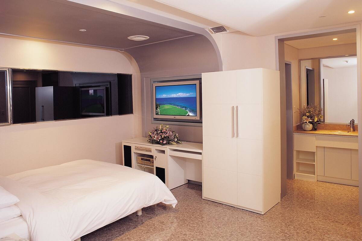 A bedroom with a bed, a desk, a TV, and a wardrobe.