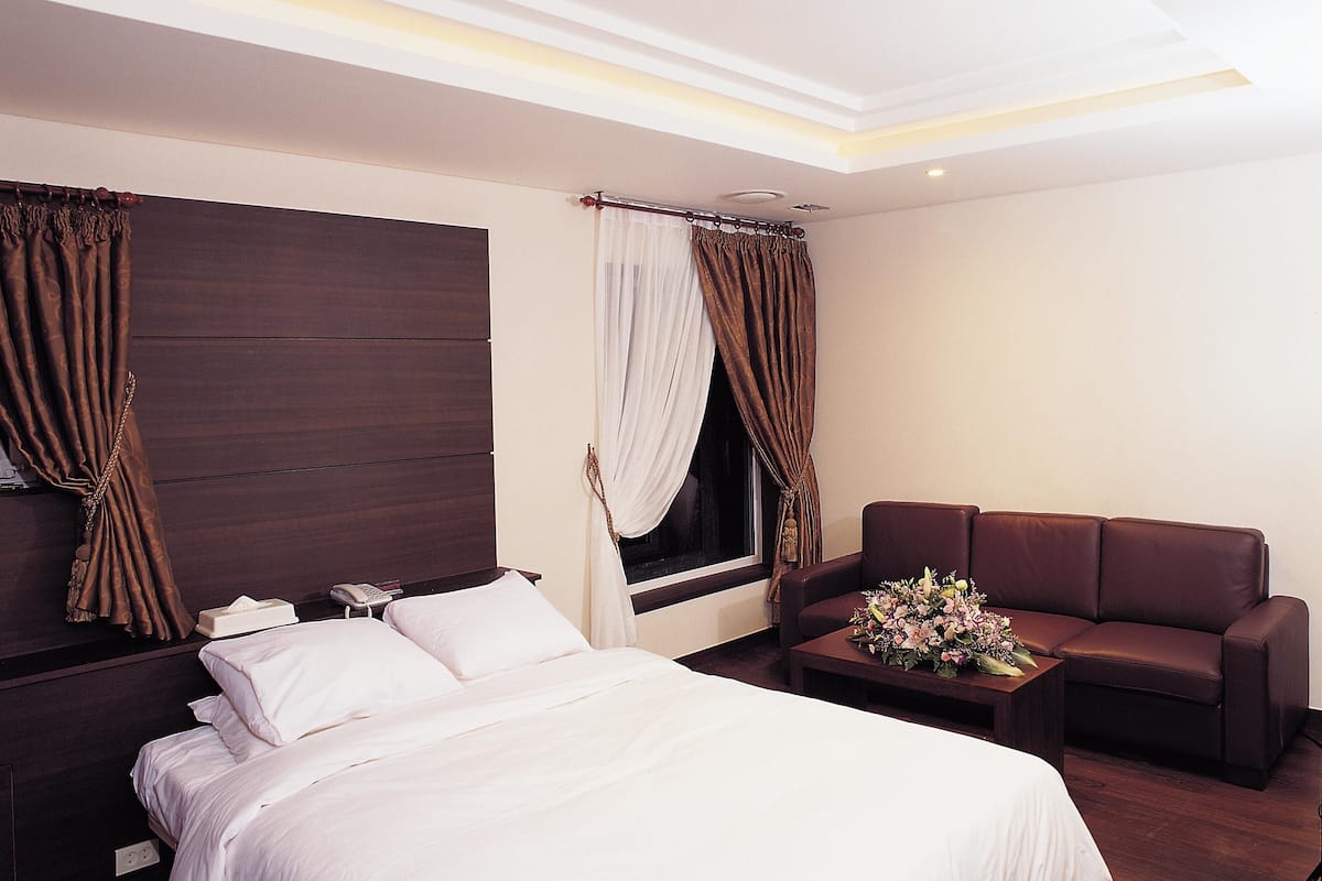 A hotel room with a bed, a sofa, a bedside table with a phone and a vase of flowers.