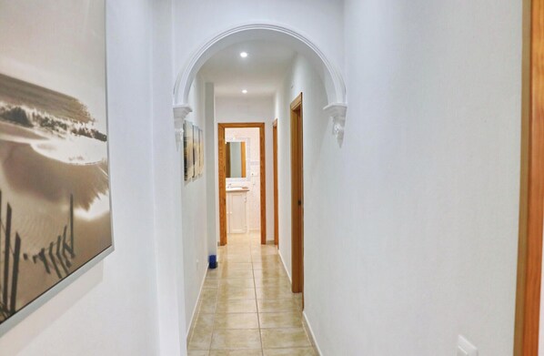 A hallway with white walls, a tiled floor, and a wooden door at the end.