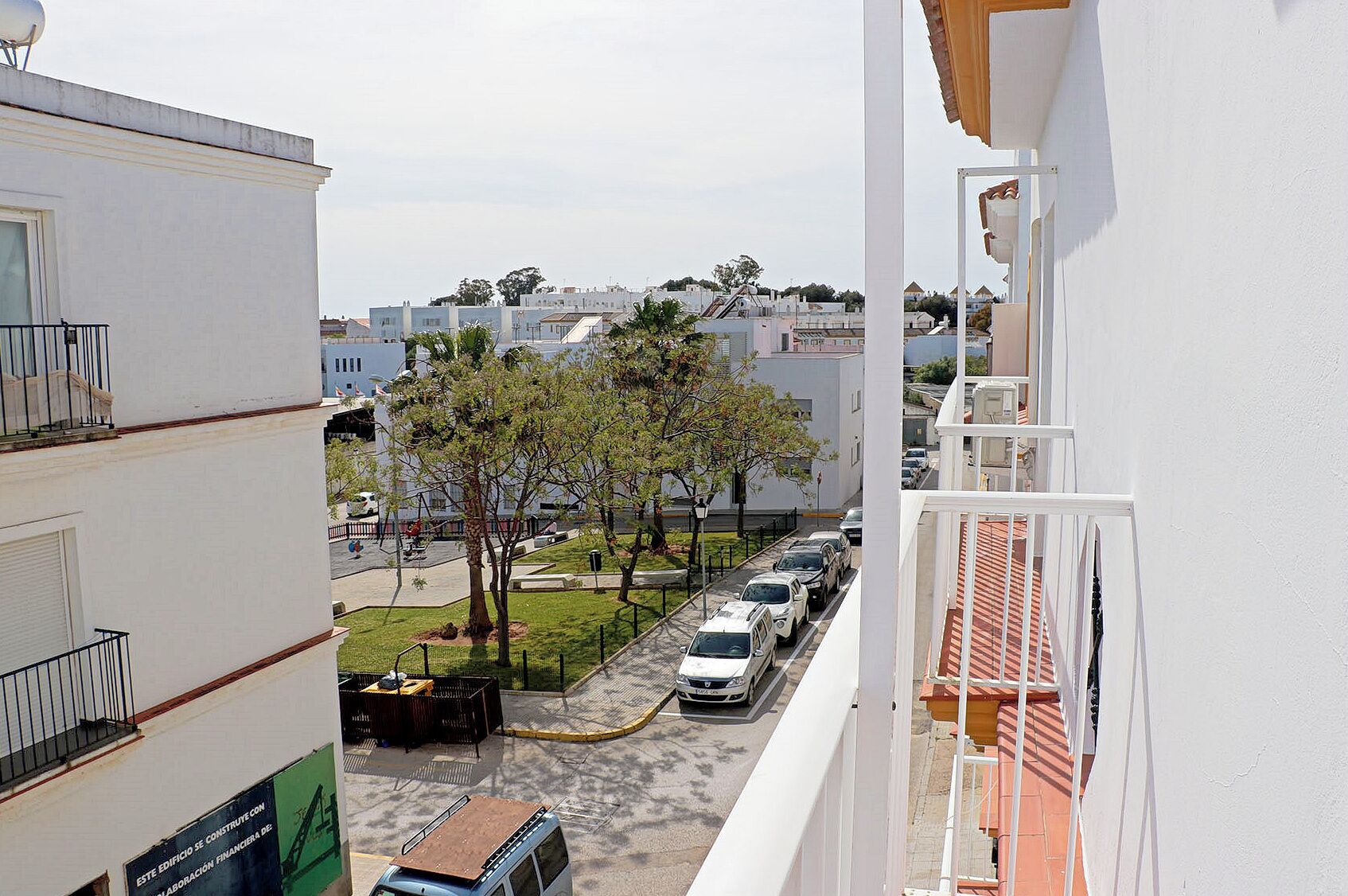 Zona residencial amb edificis blancs, un aparcament i alguns arbres.