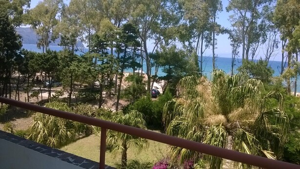 A balcony with a view of a beach, trees, and a clear sky.