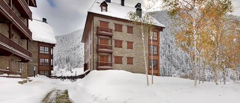 A snow-covered building with a stone facade, wooden balconies, and a snow-covered roof.