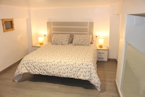 Un lit bien fait, recouvert d’une couvre-lit à motifs floraux, avec deux lampes de chevet et une tête de lit en bois.