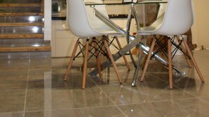 Una cocina moderna con una pared de acento de piedra, una zona de comedor con dos sillas blancas y una mesa de vidrio, y una escalera que conduce a un nivel superior.
