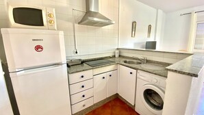 Cocina funcional con gabinetes blancos, microondas integrado, campana extractora de acero inoxidable, lavaplatos y lavadora.