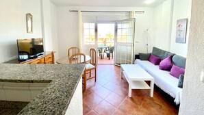 Una sala de estar con televisor, sofá, mesa de centro y un comedor con sillas.