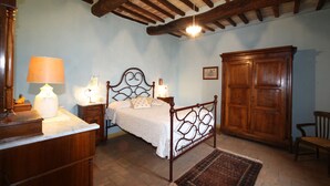 Ein Schlafzimmer mit einem hölzernen Bett, Nachttischen mit Lampen, einem Kleiderschrank und einem Schreibtisch mit einer Lampe.
