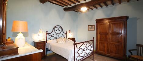 Un dormitorio con cama de madera, mesitas de noche con lámparas, un armario y un escritorio con lámpara.