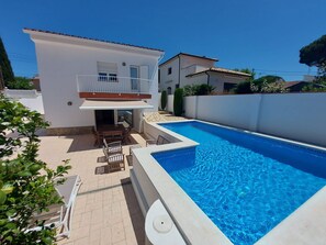 A two-story house with a swimming pool, a patio with outdoor furniture, and a white exterior.