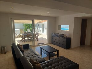 Una sala de estar moderna con un sofá, una mesa de centro, un televisor y un ventanal corredera que da a un patio exterior.