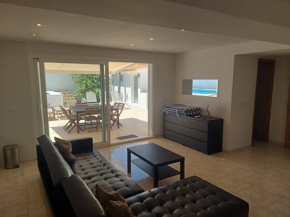 A modern living room with a sofa, a coffee table, a TV, and a sliding glass door leading to an outdoor patio.