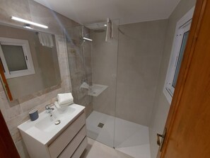 Un baño moderno con ducha de vidrio, tocador con lavamanos y espejo.
