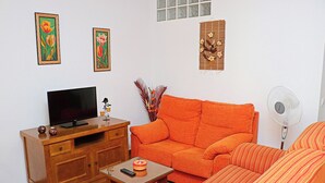 A living room with a wooden TV stand, orange sofa, and a small table with a remote control. - Two bedroom apartment in the centre (CONIL DE LA FRONTERA)