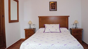 A bedroom with a wooden headboard, a floral bedspread, two bedside tables with lamps, and a framed picture on the wall. - Two bedroom apartment in the centre (CONIL DE LA FRONTERA)