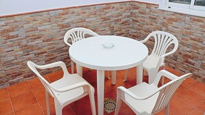 A round white table with four white plastic chairs in a corner with a stone-patterned wall and orange tiles. - Two bedroom apartment in the centre (CONIL DE LA FRONTERA)
