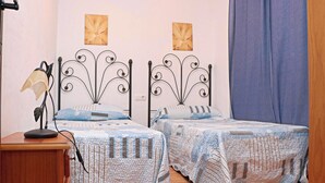 A bedroom with two beds, each with a patterned quilt, a bedside lamp, and wall-mounted flower paintings.