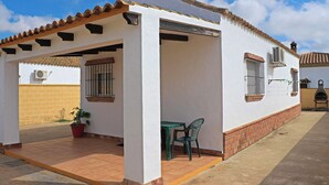 A white building with a tiled roof, a covered patio area with a table and chairs, and a potted plant.
