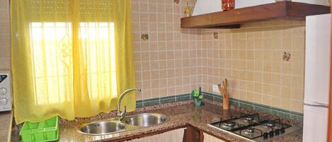 A kitchen with a gas stove, stainless steel sink, and a green dish rack.