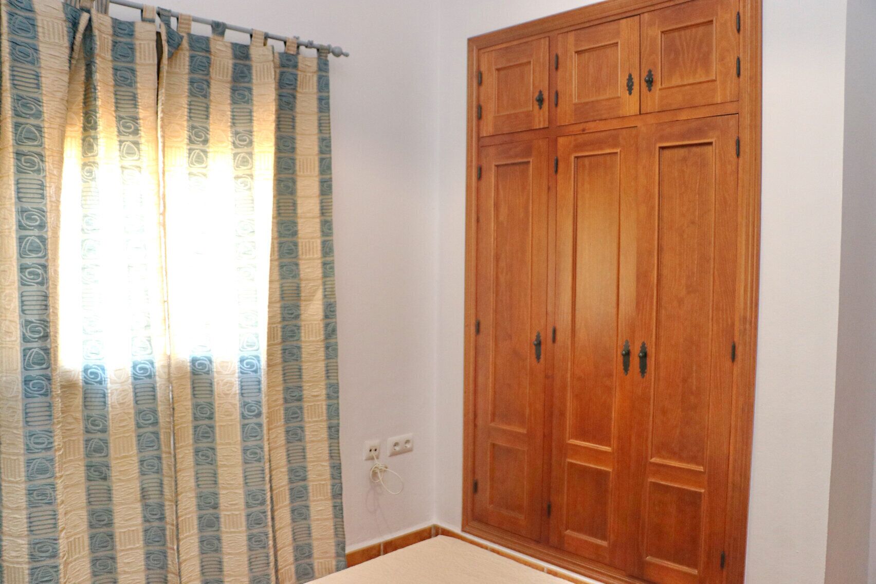 A room with a large wooden wardrobe, a patterned curtain, and a light switch on the wall.