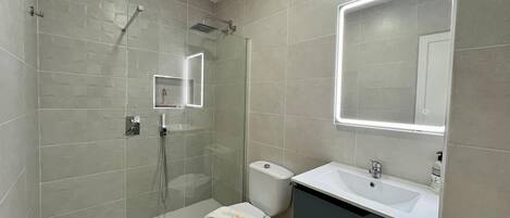 A modern bathroom with a glass-enclosed shower, a toilet, and a vanity with a mirror.