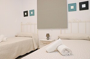 A hotel room with two beds, each with a white bedspread and matching pillows. There is a nightstand with a lamp and a folded towel on it. The walls have two framed pictures, one black and one teal. - Rural apartment for four people (CONIL DE LA FRONTERA)