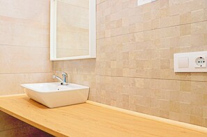 Une salle de bain avec un lavabo rectangulaire, un miroir et une prise électrique murale.