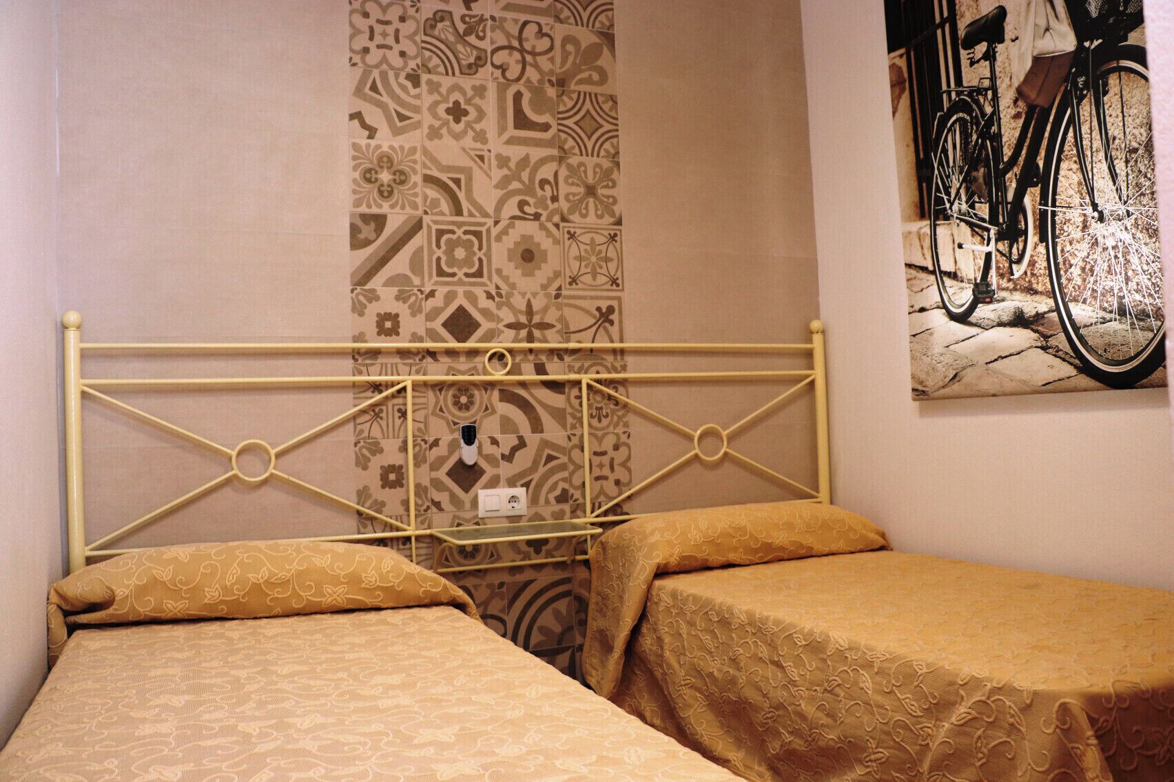 A room with a metal bed frame, patterned wallpaper, and a bicycle painting on the wall.
