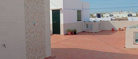 A rooftop terrace with red tiles, a green door, and potted plants.