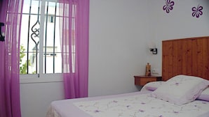 A bedroom with a bed, a nightstand, a window with purple curtains, and a wooden headboard. - Central apartment with air conditioning (CONIL DE LA FRONTERA)
