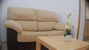 A beige sofa with a textured fabric, a wooden coffee table, and a white vase with white flowers. - Central apartment with air conditioning (CONIL DE LA FRONTERA)