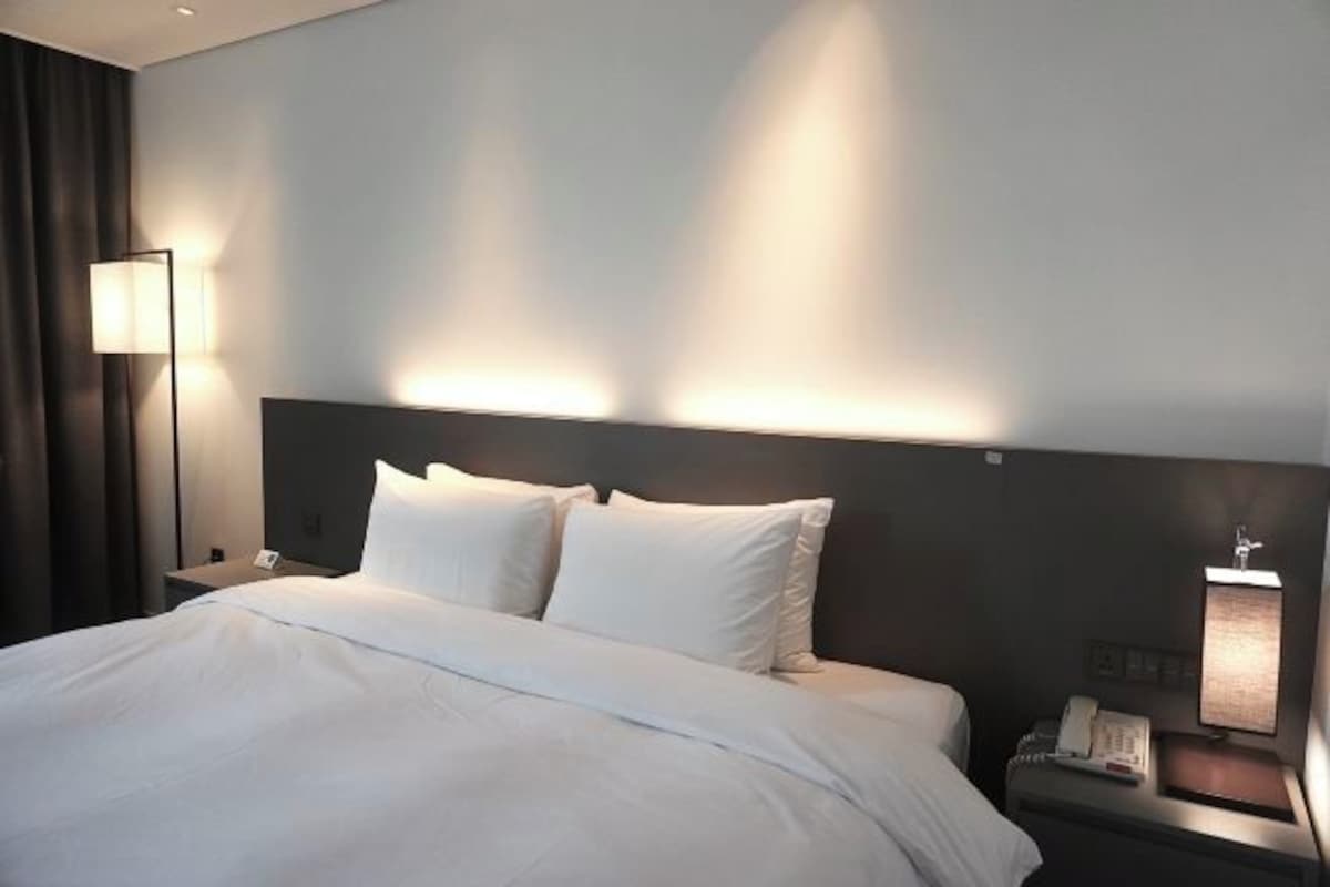 Una habitación de hotel con una cama grande, una mesita de noche con lámpara y un teléfono.