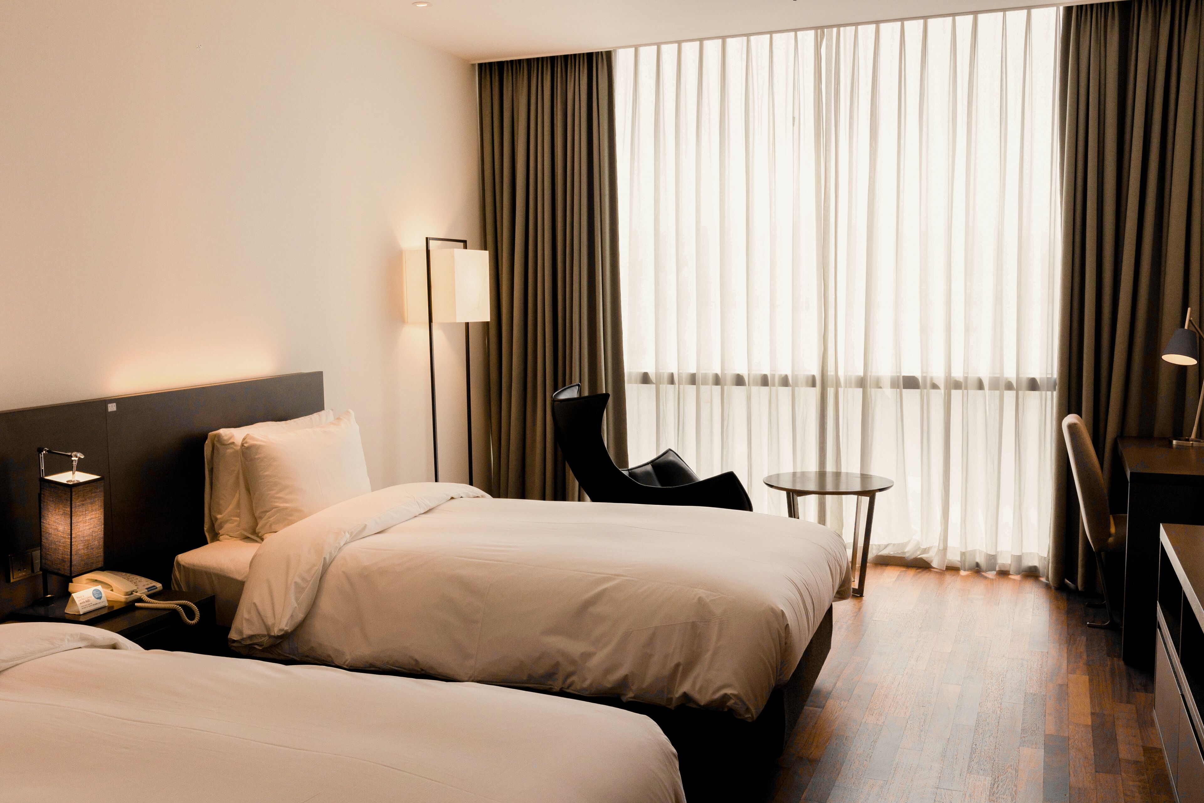 A hotel room with two beds, a desk, a chair, a lamp, and a phone on the nightstand.