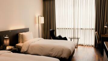A hotel room with two beds, a desk, a chair, a lamp, and a phone on the nightstand.
