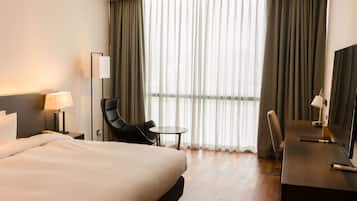 A hotel room with a bed, a desk, a chair, a TV, and a window with curtains.