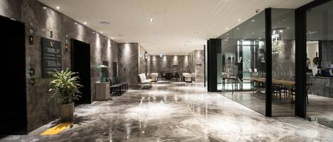 A spacious lobby with marble flooring, seating areas, and glass walls.