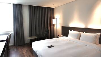 A hotel room with a large bed, a desk, a chair, and a lamp.
