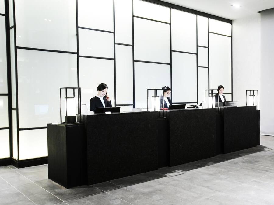 Una recepción con tres empleados, un interior moderno con ventanas amplias y un suelo de baldosas.