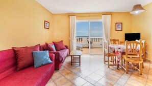 A living room with a red sofa, a wooden dining table, and a TV. - Attic apartment with stunning sea views (Costa Calma (Fuerteventura))