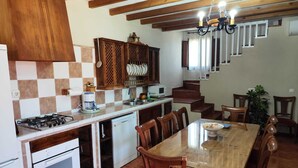 A kitchen with a gas stove, dishwasher, and wooden cabinets. There is a dining table with chairs and a chandelier above. - 6 bedroom holiday house in Almachar (ALMACHAR)