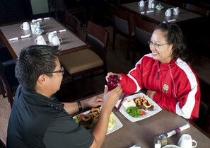 Uma área de refeições com mesas preparadas para dois, cada uma com pratos de comida, talheres e acompanhamentos.