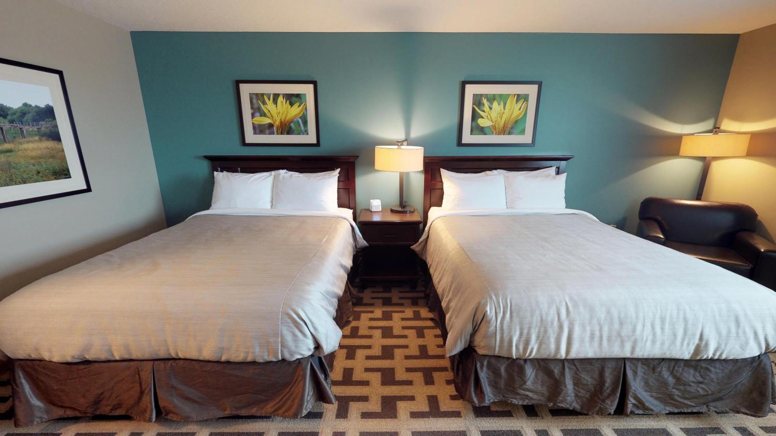 A hotel room with two beds, a patterned carpet, and two wall-mounted lamps.