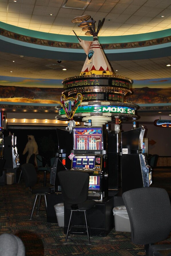 Un casino avec des machines à sous, un panneau au néon indiquant « SMOKE SIG », et un grand plafond décoré.